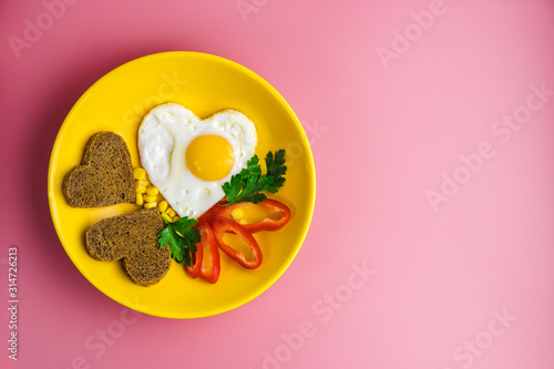 heart-shaped fried egg and bread in a yellow plate on a red background. valentines day concept