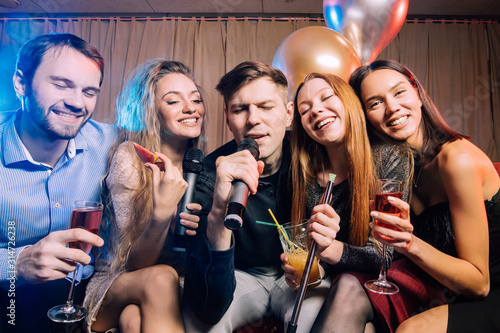 happy cheerful adults, women and men spending day-off in karaoke bar, young ladies and guys wearing party clothes, dresses. energetic and emotional group of people have fun