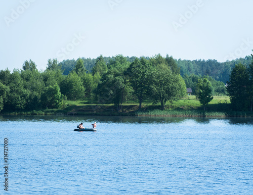 a large, wide river and in the middle is a boat with two anglers; on the other side are trees, houses and forest