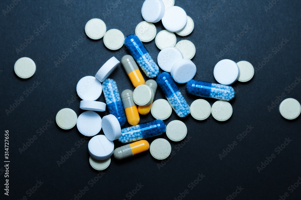 Heap of colorful pills, pharmaceutical medicine tablets and capsules over black background.