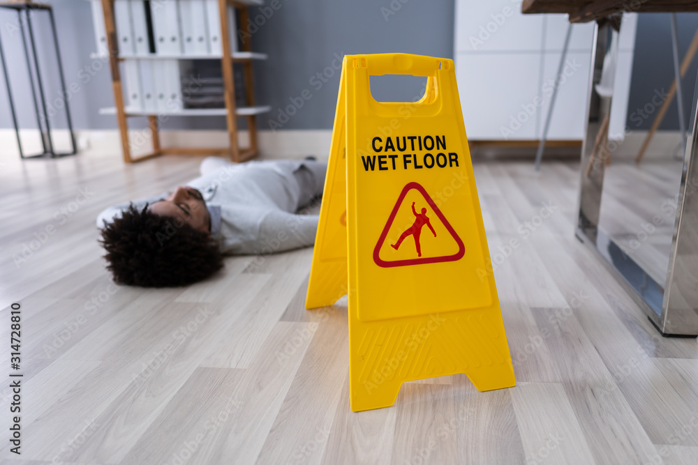 Man Falling On Wet Floor In Front Of Caution Sign - obrazy, fototapety, plakaty 