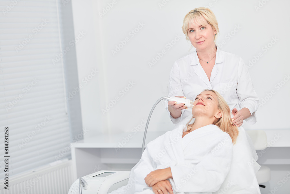 Fototapeta premium talented experienced cosmetologist improving the face of female blonde client, looking at the camera.job, professsion, occupation