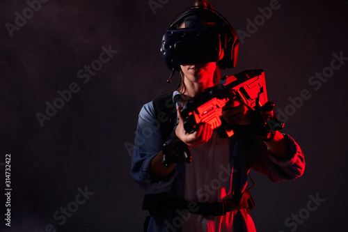 Young girl killer using technology as vr headset, goggles, weapons playing shooter game. Isolated smoky background, neon light
