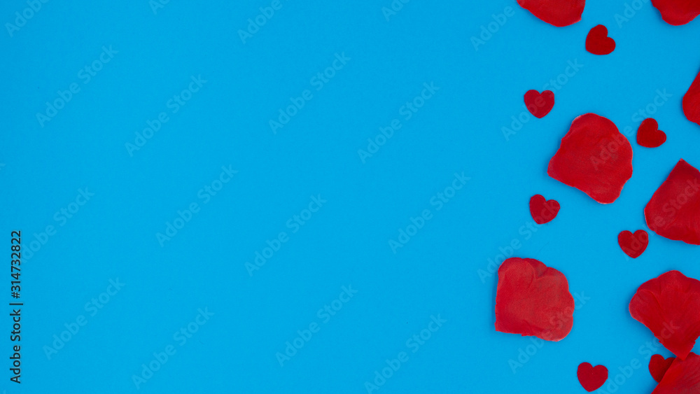 Red rose petals and red hearts lying on a blue background.