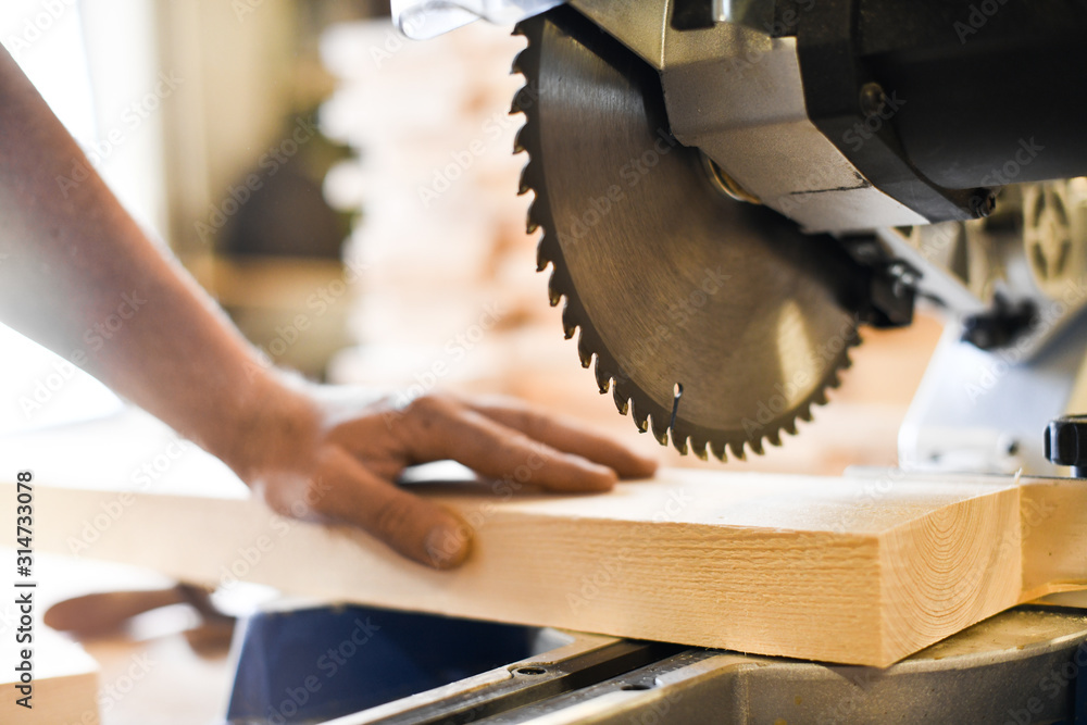 Worker hands details of wood cutter machine with a circular saw and wooden  board. Circular cutting saw in action. Stock Photo