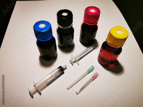 tubes of paint and brushes Refill inks for printers and copiers with blue, red, yellow and black ink in bottles with syringes to pull on and needles on a white background and black background