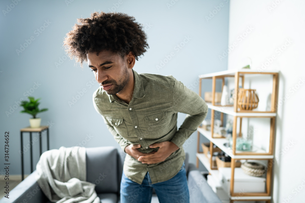 Man With Stomach Ache Standing Near Couch At Home