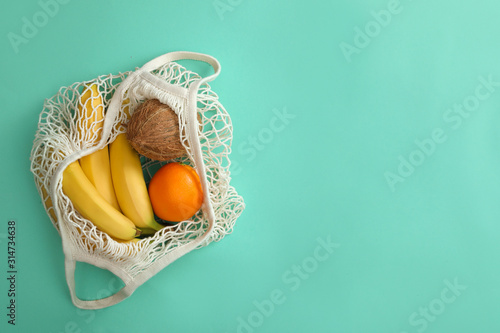 Net bag with fruits on turquoise background, top view. Space for text