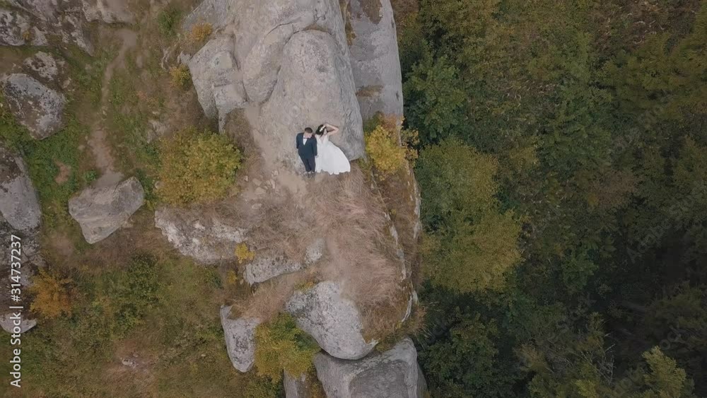 Newlyweds stand on a high slope of the mountain. Groom and bride. Aerial view Newlyweds stand on a high slope of the mountain. Groom and bride. Aerial view
