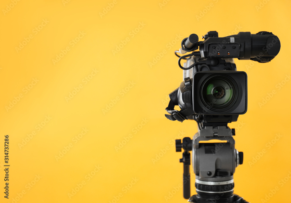 Modern professional video camera on yellow background. Space for text