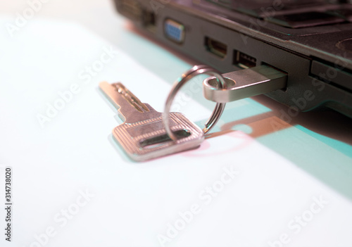 The key to the lock and a flash drive on the USB output of the laptop. White background.