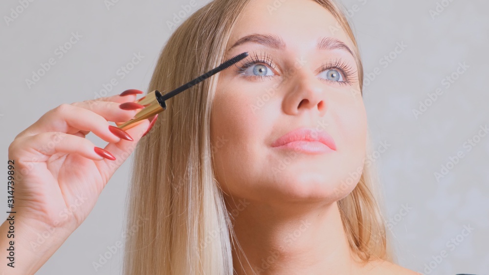 Fototapeta premium Headshot of female with bright makeup applying mascara on eyelashes.