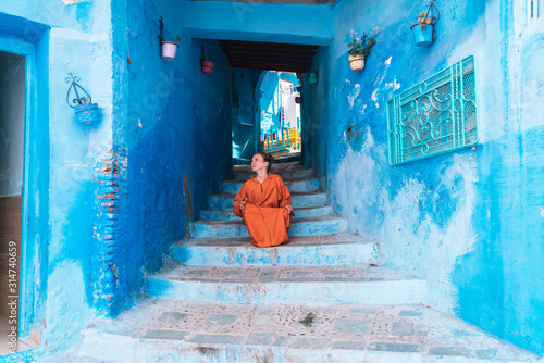 in a tunnel of the blue city of Morocco, a girl in a bright orange dress sits on the steps leading up © nelen.ru