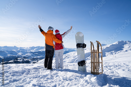 Young Couple Standing Near Snowboard And Sledge In Snow