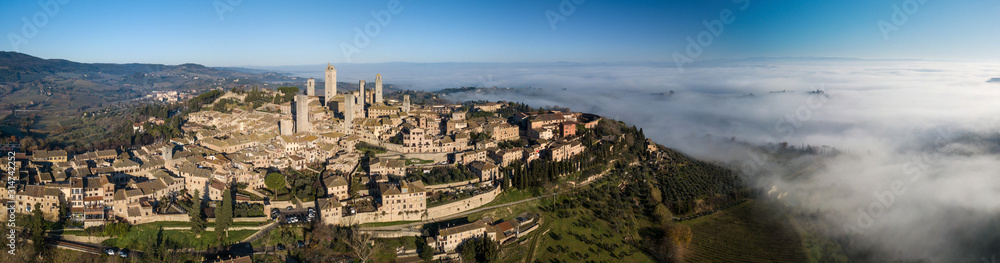 Big drone aerial landscape panorama of the wonderful village of San Gimignano a small walled medieval hill town in the province of Siena, Tuscany in morning mystic fog.