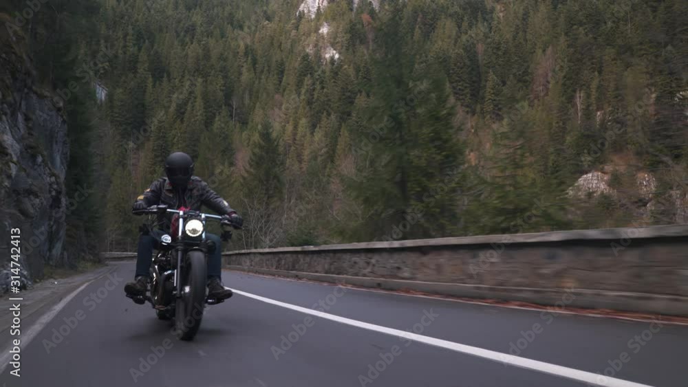 Rolling shot of a motorcycle young man riding on a mountain road during fall Rolling shot of a motorcycle young man riding on a mountain road during fall