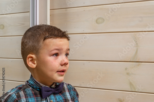 Foto A 4 years old boy in a blue clerical shirt is crying on a light wooden background