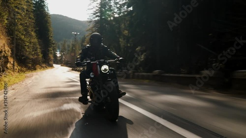 Rolling shot of a motorcycle man riding fast a vintage motorcycle on a mountain road on a sunny day during fall photo