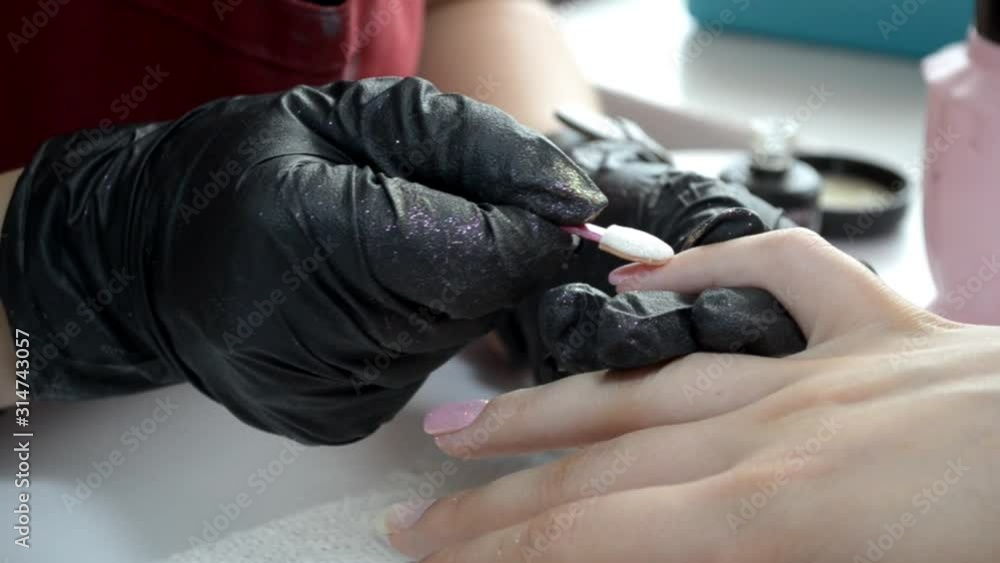 Manicurist applies a brilliant rub on a nail covered with pink gel polish Manicurist applies a brilliant rub on a nail covered with pink gel polish