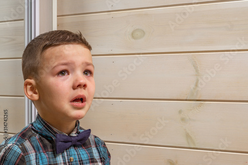 Foto A 4 years old boy in a blue clerical shirt is crying on a light wooden background