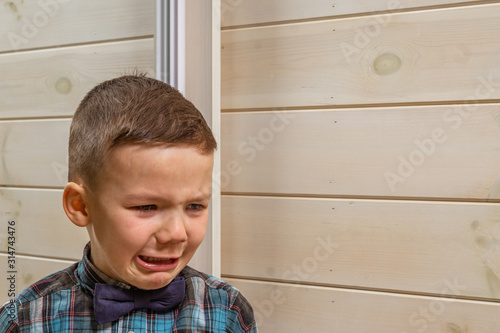 Foto A 4 years old boy in a blue clerical shirt is crying on a light wooden background