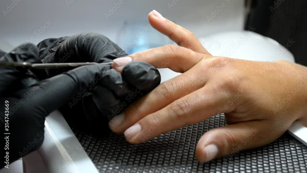 Manicure master in black gloves cuts a cuticle from a client finger with thin nail scissors Manicure master in black gloves cuts a cuticle from a client finger with thin nail scissors
