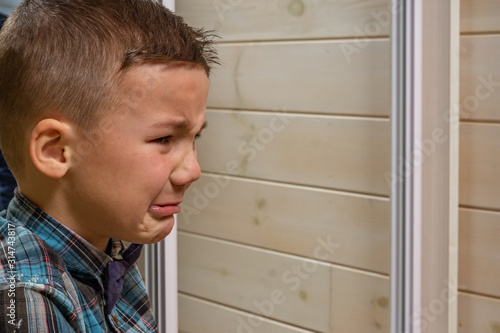 Bild auf Leinwand A 4 years old boy in a blue clerical shirt is crying on a light wooden background
