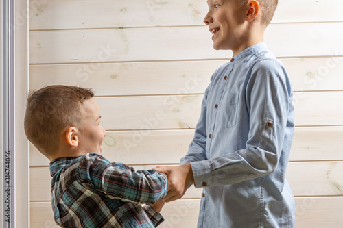 A 4-year-old boy in a blue klepy shirt cries on a light wooden background and his brother, 10 years old, is standing. photo