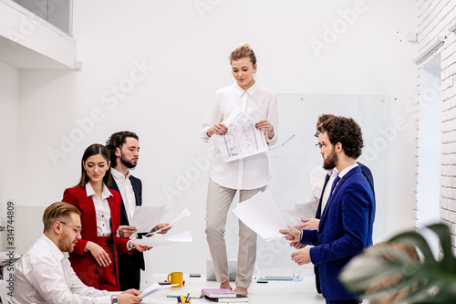young business people enjoy, happy together in business office, after meeting, completion of business project, co-workers in formal wear. lady in white stand on table with papers