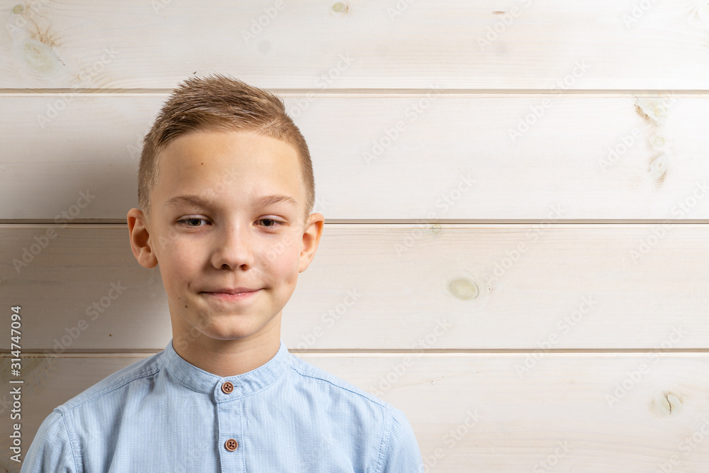 A boy of 10 years old in a blue shirt smiles on a light wooden background and makes various signs with his hands. A boy of 10 years old in a blue shirt smiles on a light wooden background and makes various signs with his hands.