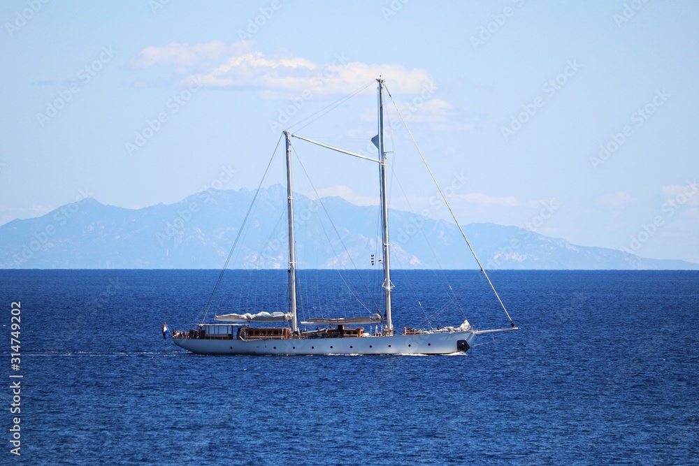 Yacht without raised sails on the background of the island follows in the Mediterranean Sea in September 2019 Yacht without raised sails on the background of the island follows in the Mediterranean Sea in September 2019