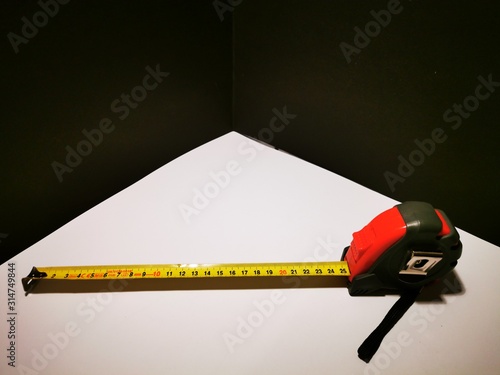 A tape measure for rolling in and out with fixed function in a red black case and a yellow measuring bar with black numbers on a white background