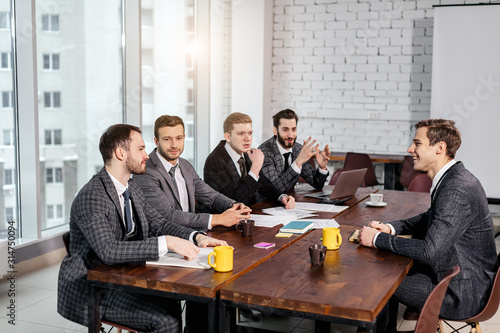 positive business team consisted of young men leaders in tuxedo gathered in office to discuss business ideas and strategies, happy to be a part of successful team. business coworking concept