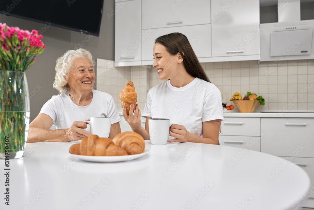 Senior woman laughing with granddaughter in kitchen.