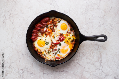 Hot homemade fried eggs with tomatoes and sausage in a pan top view
