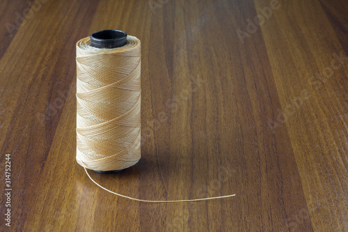 spool of beige thread on a yellow wooden table surface