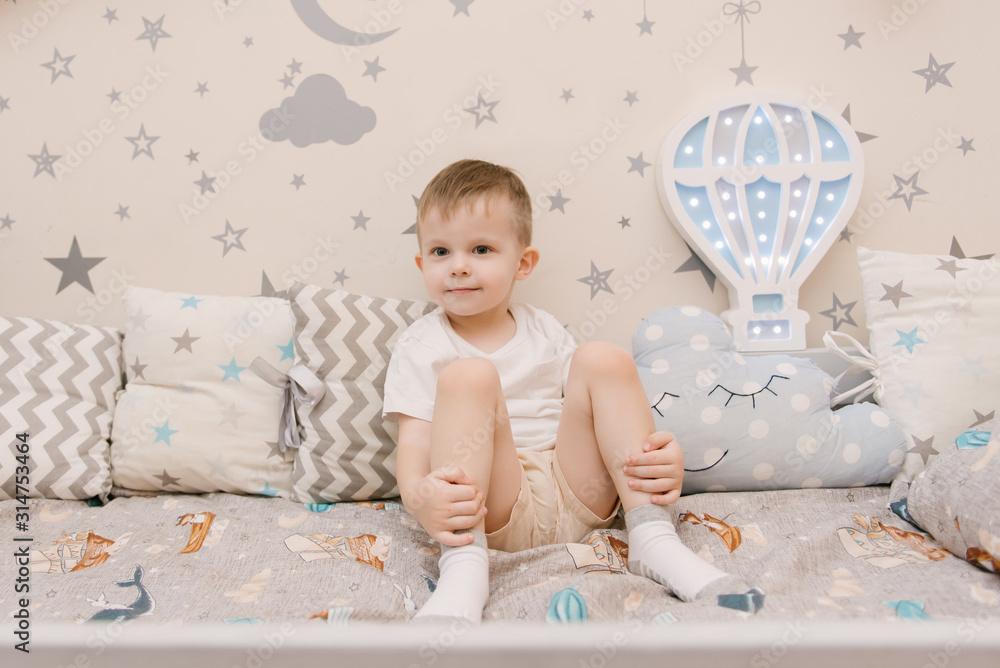 Little cute baby boy sitting in the children room in a wooden bed house with night lights in the shape of a balloon