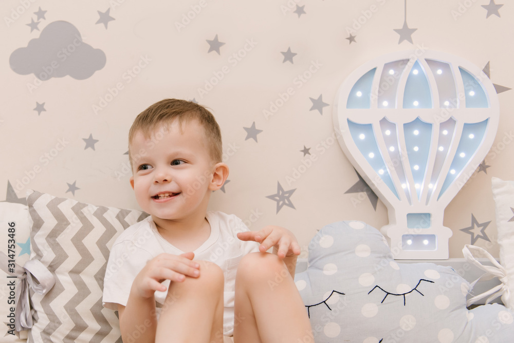 Little cute baby boy sitting in the children room in a wooden bed house with night lights in the shape of a balloon Little cute baby boy sitting in the children room in a wooden bed house with night lights in the shape of a balloon
