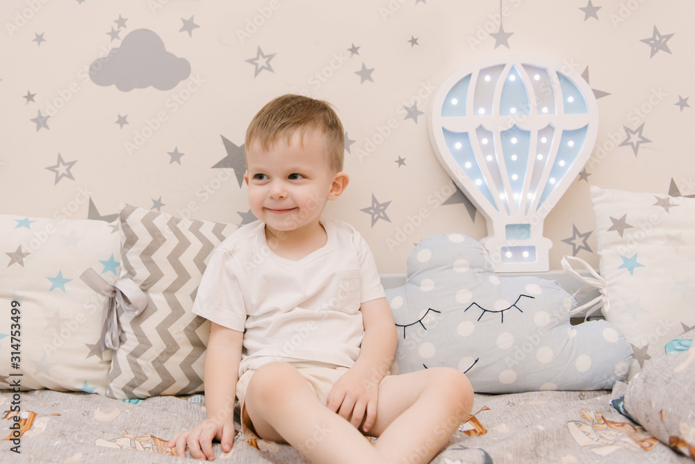 Naklejka premium Little cute baby boy sitting in the children room in a wooden bed house with night lights in the shape of a balloon