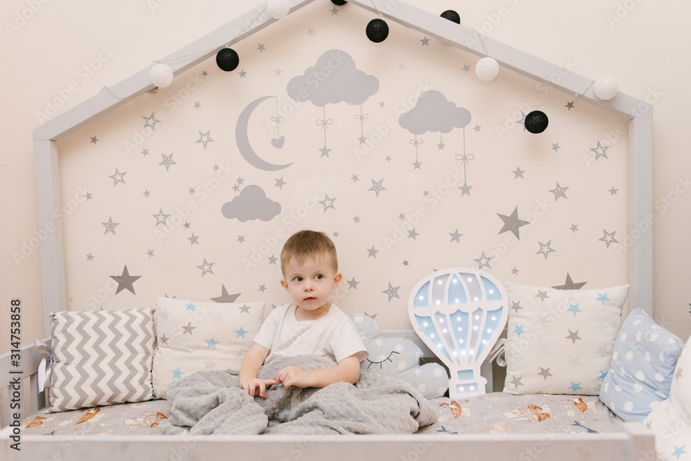 Little cute baby boy sitting in the children room in a wooden bed house with night lights in the shape of a balloon