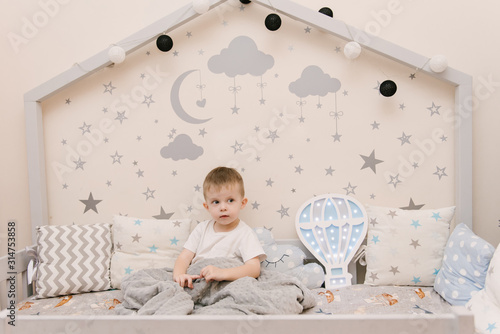 Obraz na płótnie Little cute baby boy sitting in the children room in a wooden bed house with night lights in the shape of a balloon w salonie