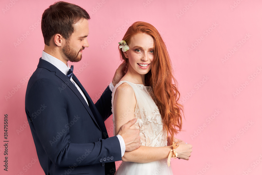 Man wearing elegant suit cutely look at woman with red auburn hair with flower. Bearded man straighten hair isolated over pink background Man wearing elegant suit cutely look at woman with red auburn hair with flower. Bearded man straighten hair isolated over pink background