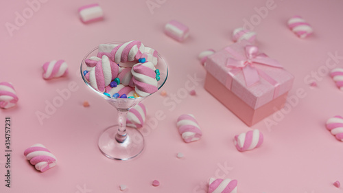 Lots of pink marshmallows on a pink background next to a pink gift box with a surprise inside. Valentine's day.