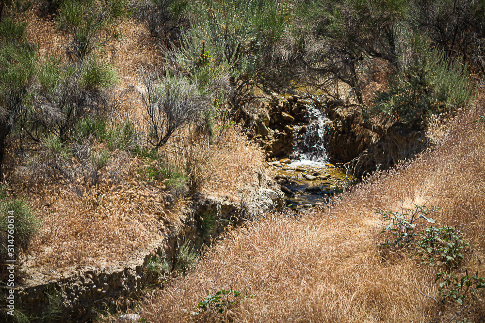 small stream of water falling into timy pool in scrub desert small stream of water falling into timy pool in scrub desert