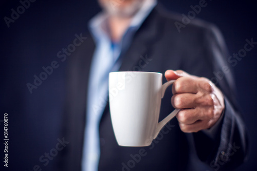 Businessman in suit holding cup of tea or coffee in hand in front of black background