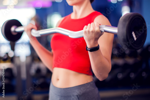 Woman in red top training bicep in gym. People, fitness and lifstyle concept