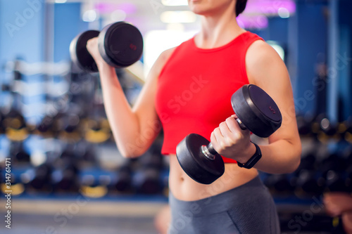 Woman in red top training bicep with dumbbels in gym. People, fitness and lifstyle concept