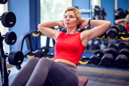 Woman in red top training abs in gym. People, fitness and lifstyle concept