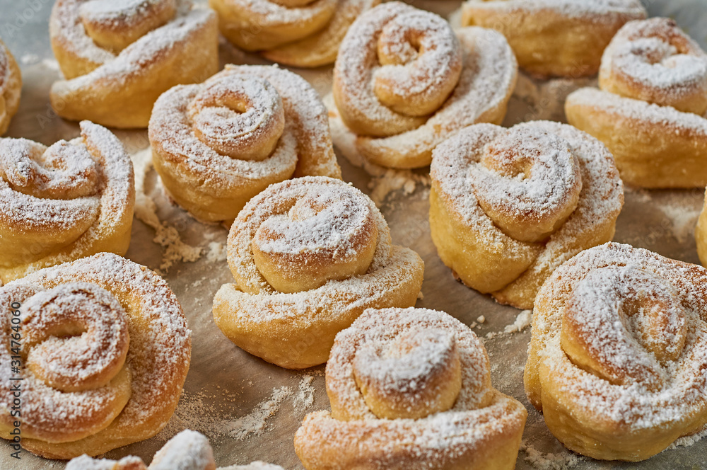 Many homemade baked buns in form of rose spangled of powdered sugar on paper. Confectioners workplace. Close-up Many homemade baked buns in form of rose spangled of powdered sugar on paper. Confectioners workplace. Close-up