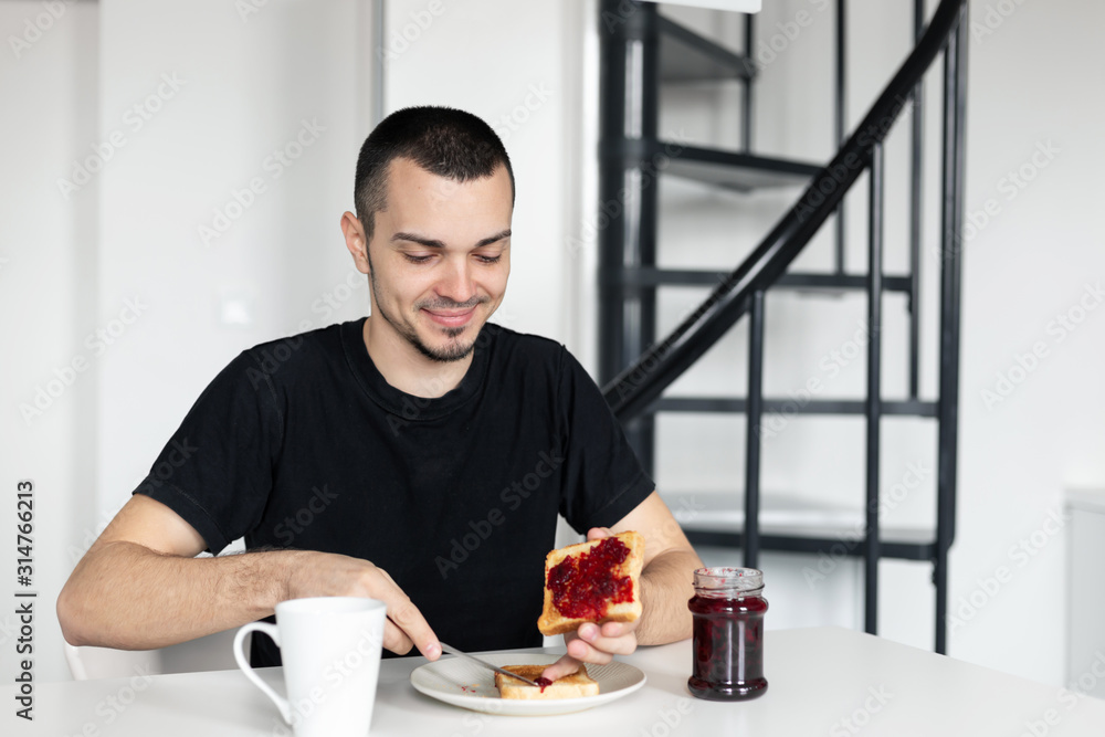 The guy has breakfast with toast with jam. The guy has breakfast with toast with jam.